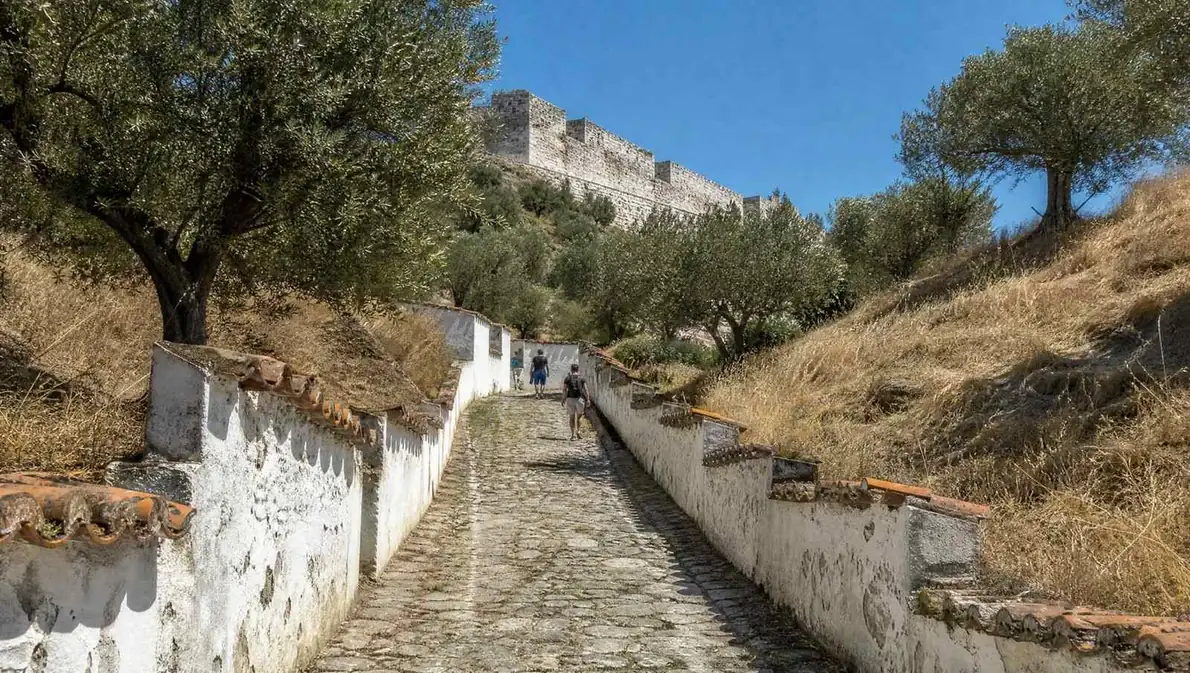 Eine gepflasterte Gasse, die zwischen weiß getünchten Mauern zu einem Hügel hinaufführt